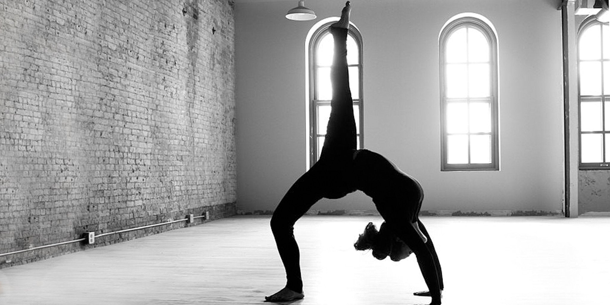 Woman in activewear balances in Tip Toe Bow yoga pose indoors