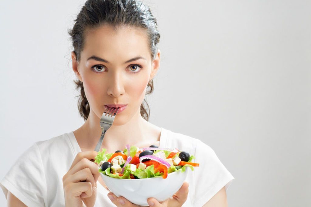 Smiling woman holding a salad, representing women's health and wellness focus